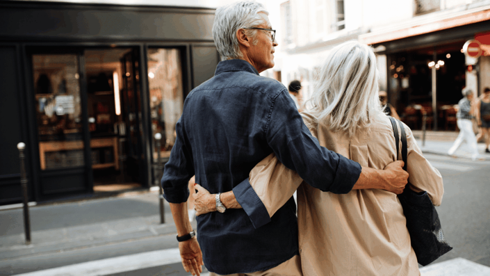 A senior couple with gray hair walks arm-in-arm down a city street, with storefronts in the background, symbolizing a comfortable retirement and the importance of effective retirement planning.
